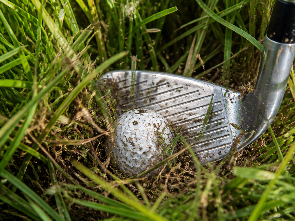 Golf ball buried in punishing U.S. Open rough during a difficult recovery shot.